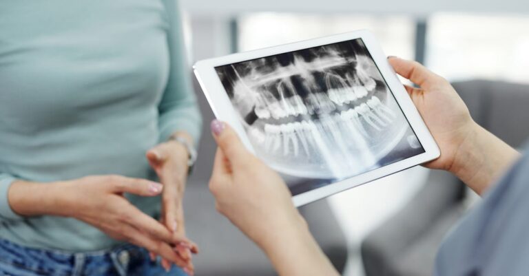 A dentist displays a dental x-ray on a tablet to a patient during a consultation.